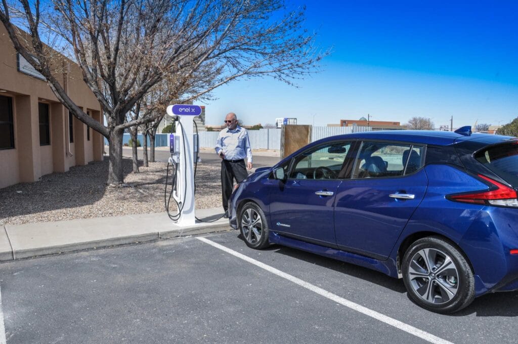 a man standing next to an EV charging station while charging his car.